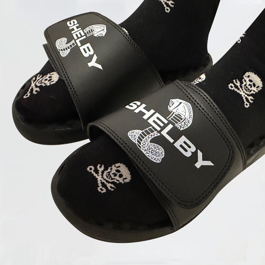 Close up of two feet wearing Shelby sandals and skull-and-wrench graphic socks
