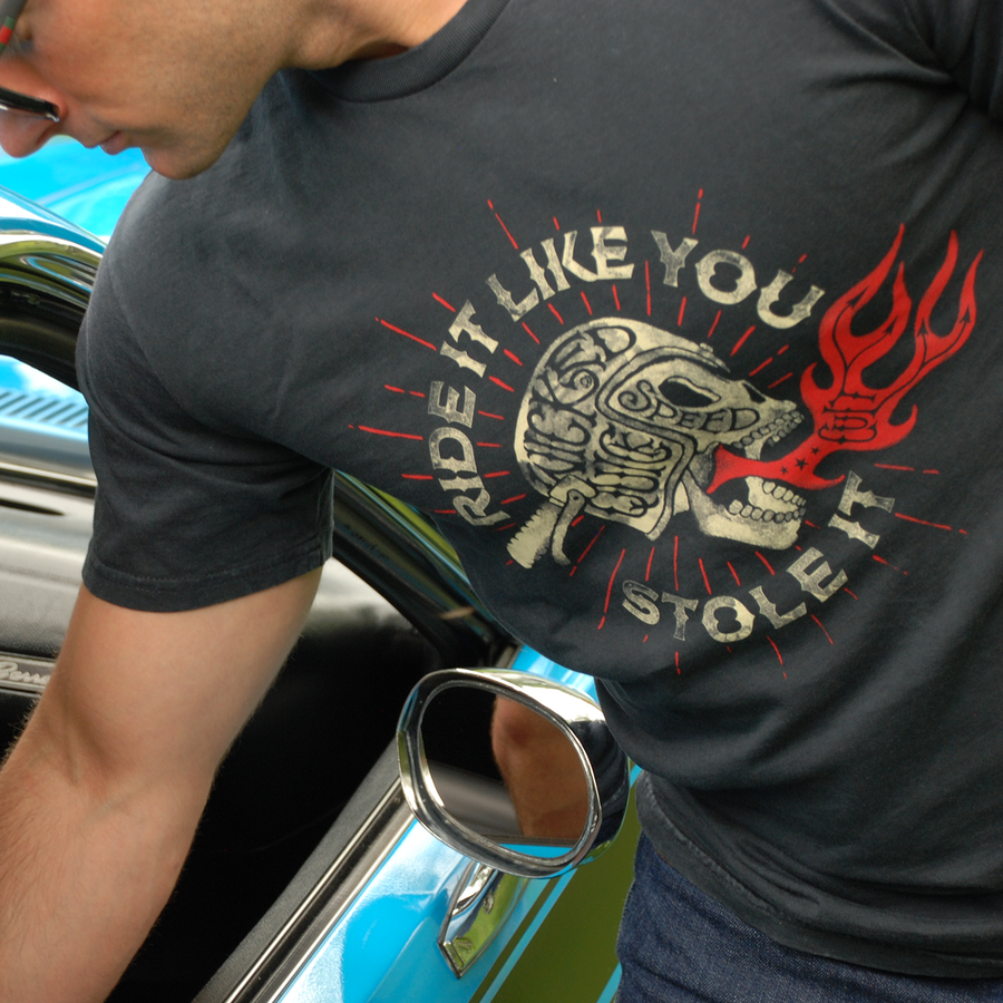 Man wearing a Ride It Like You Stole It black graphic shirt by Wicked Quick while looking at a muscle car