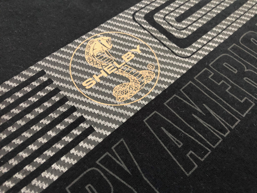 Close up of a Gold Shelby Cobra logo on a black graphic shirt